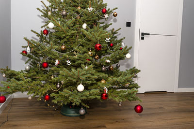 A spruce christmas tree decorated with baubles standing in the hall of a modern house. christmas 