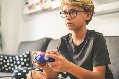 Boy playing video game while sitting on sofa in living room at home