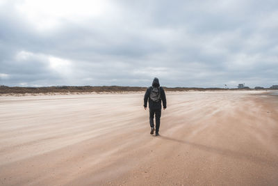 Rear view of man walking on beach against sky