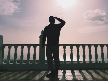 Man standing on railing by sea against sky