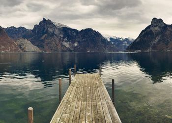 Pier over lake by rocky mountains against sky