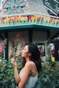 Side view of young woman standing against pink flowering plants
