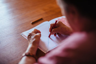 From above senior woman with alzheimer's mental health issues painting on a notebook inside her home