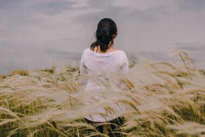 Rear view of woman standing amidst plants against cloudy sky