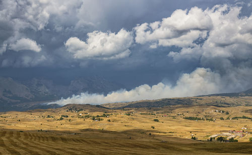 Dry grass fields with smoke from burned grass and heavy rainy clouds in the sky. 