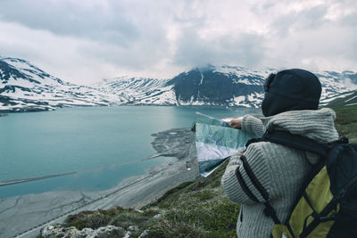 Woman with map standing at lakeshore against mountains during winter