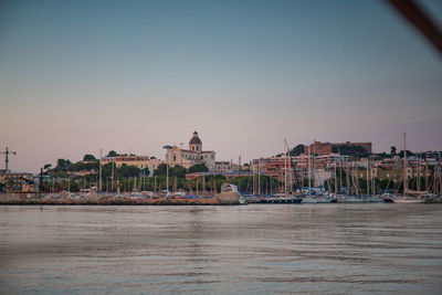 Sailboats in sea by buildings against clear sky