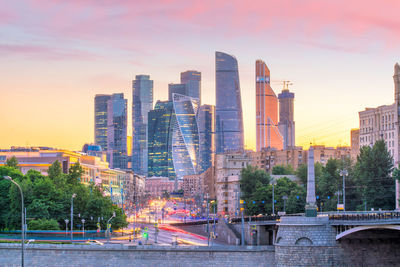 City buildings by river against sky during sunset