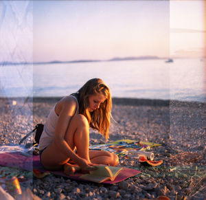 Young woman sitting on beach against sky during sunset