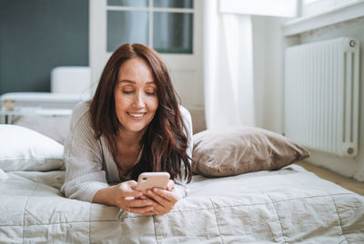 Young woman using mobile phone while sitting on bed at home