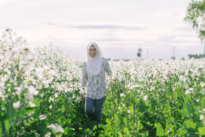 Woman standing by flowering plants on field