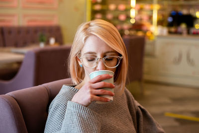 Young attractive blonde girl in cafe drinks coffee from a paper cup and relaxes