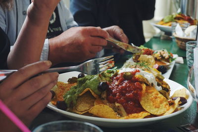 Cropped image of hands holding fork and table knife on food plate over table