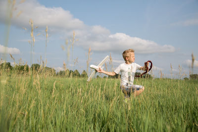 Boy playing with toy airplane on field against sky