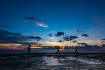 Silhouette people on beach against sky during sunset