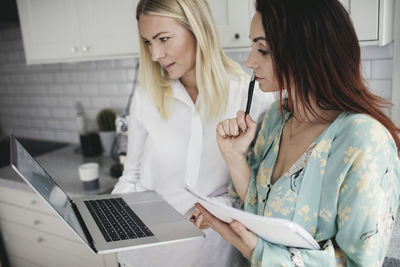 Female colleagues discussing over laptop in kitchen at home