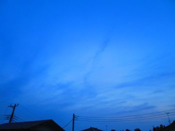 Low angle view of silhouette electricity pylon against blue sky