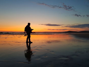 Silhouette man standing on beach against sky during sunset