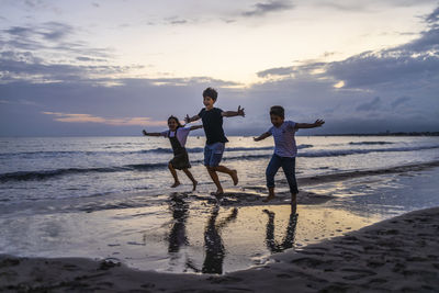 Siblings with arms outstretched running at beach during sunset