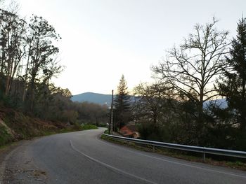 Country road by trees against clear sky