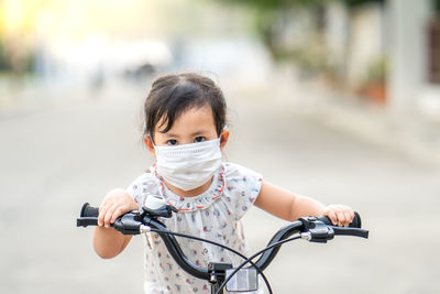 Little girl wearing medical mask prevent flu, pollutions and convid-19 riding bicycle outdoor.