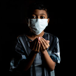 Portrait of young man standing against black background