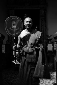 Portrait of monk holding award while standing in darkroom