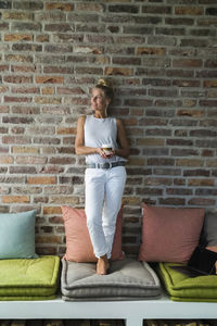 Mature woman standing on couch, drinking coffee