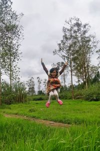 Full length of girl jumping on grass against sky