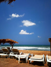 Deck chairs on beach against sky