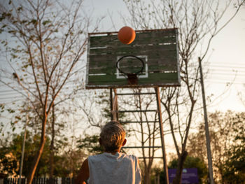 Rear view of senior man playing basketball at sunset