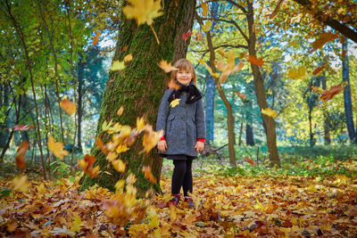 Full length of girl standing by tree in forest during autumn