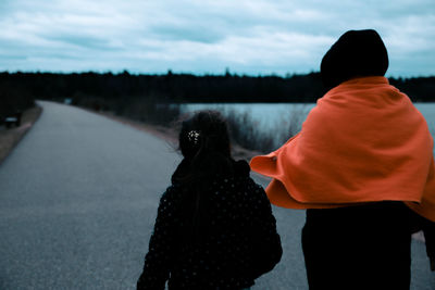 Rear view of mother and daughter standing on road during sunset