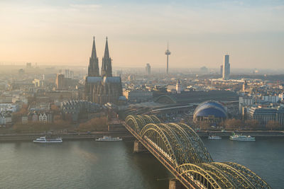 Bridge over river by buildings in city against sky