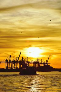 Silhouette cranes at commercial dock against sky during sunset