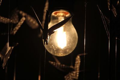 Close-up of illuminated lighting equipment hanging against black background