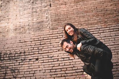 Portrait of young couple standing against brick wall