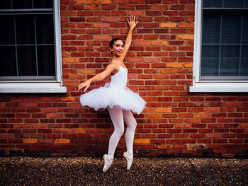 Portrait of ballerina standing against brick wall