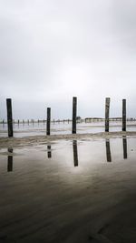 Wooden posts on sea against sky