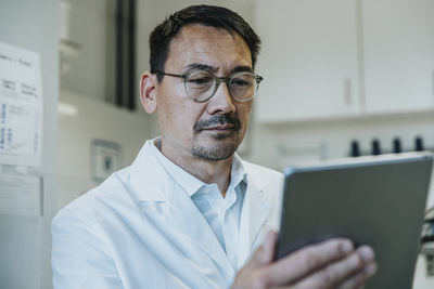 Scientist wearing eyeglasses working on digital tablet while standing at laboratory