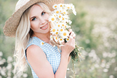 Portrait of smiling woman holding flowers in field