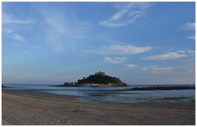 Towards st michaels mount from the sandy beach with some reflection. l blue sky with wispy cloud.