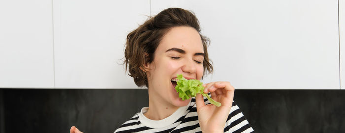 Portrait of smiling young woman holding food against wall