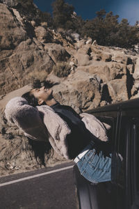 Happy young woman sitting on off-road vehicle's window at desert during sunny day