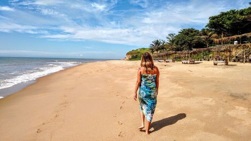 Rear view of woman at beach against sky