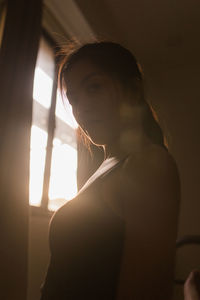 Portrait of young woman looking away by window at home