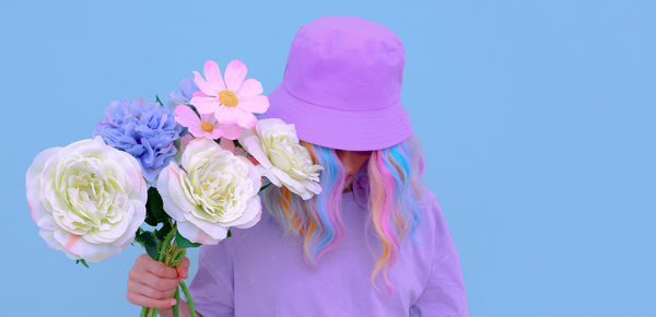 Woman wearing cap holding flowers against colored background