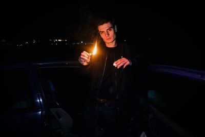 Portrait of man holding burning match at night