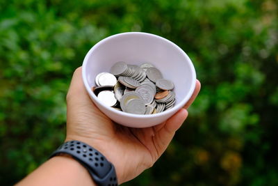 Close-up of cropped hand holding bowl with coins