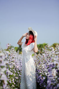 Woman wearing hat while standing amidst plants against clear sky